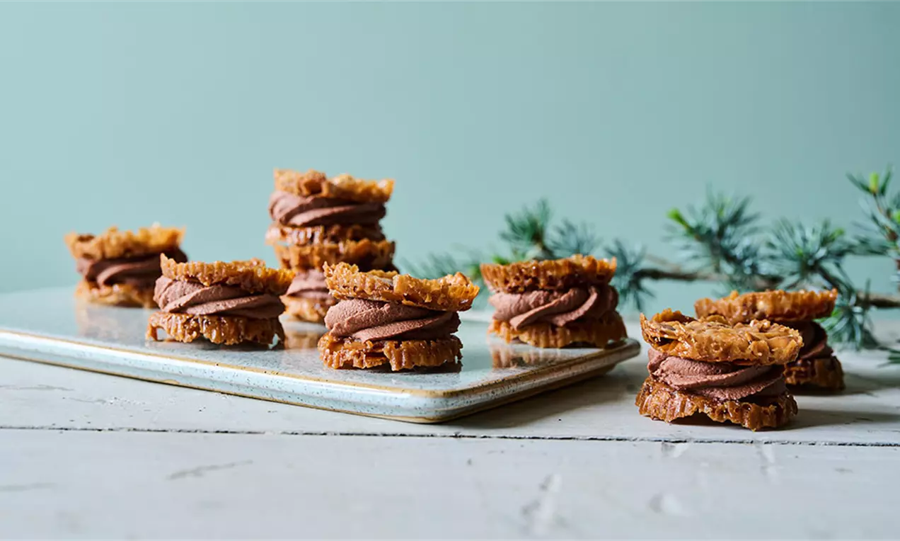 Florentiner med gyldne, knasende overflader samlet med blød, brun chokoladesmørcreme på en lys porcelænstallerken med grangrene