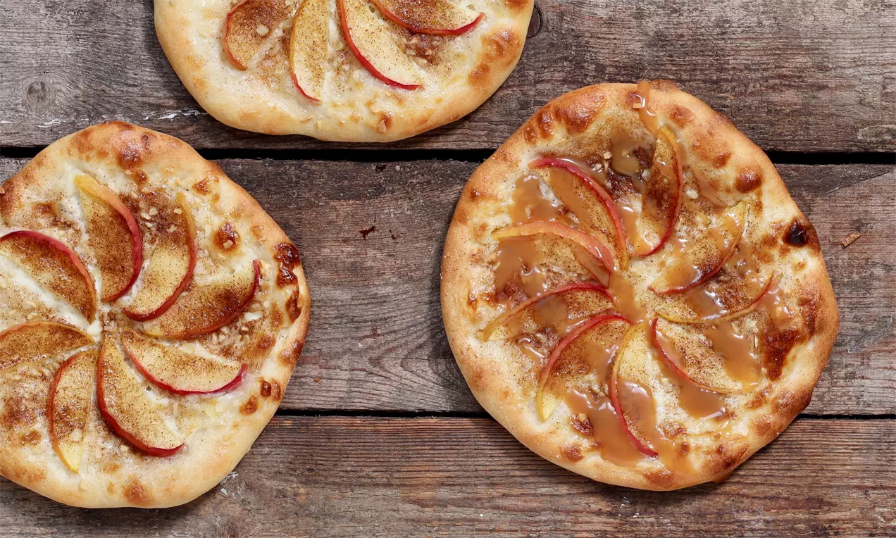 Små runde dessertpizzaer med lysebrun sprød skorpe, karamelliseret fyld og tynde røde æbleskiver arrangeret i strålemønster