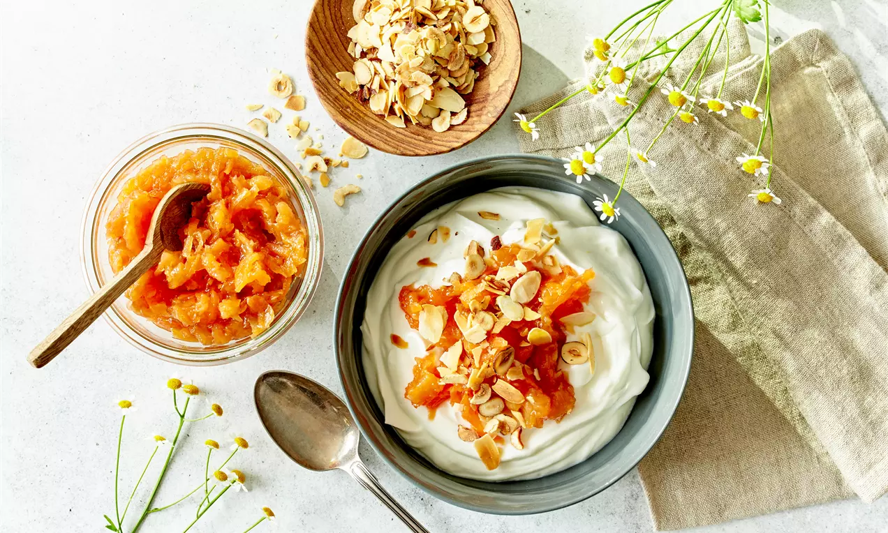 Fersken-gulerodssylt med ingefær og citron i glaskrukke med træske, lyse orange og rustik, ved siden af yoghurt toppet med sylt og ristede nødder