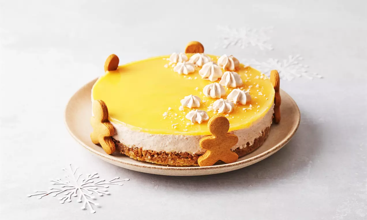 Julecheesecake med gylden appelsingelé på toppen, flødeskumspynt og honningkagefigurer rundt langs kanten på en beige tallerken