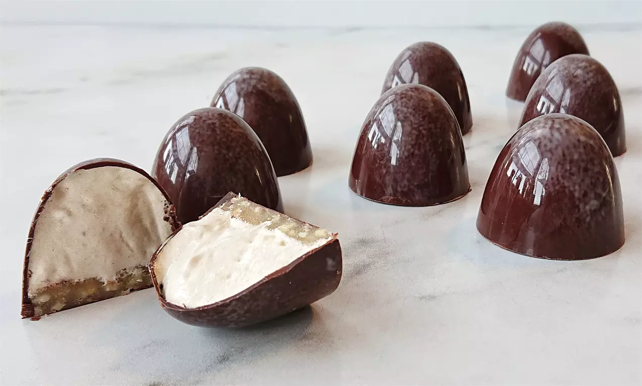 Støbte flødeboller med glat, mørk chokoladeoverflade og blødt kaffeskumfyld, placeret på lys bordplade med én flækket