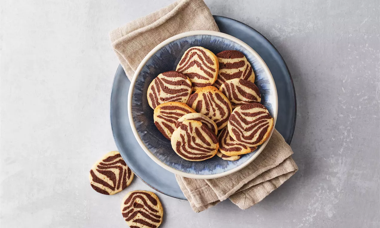 Stribede småkager med brun chokolade og lys pebermynte på en blå skål med beige stofserviet mod en lys grå baggrund