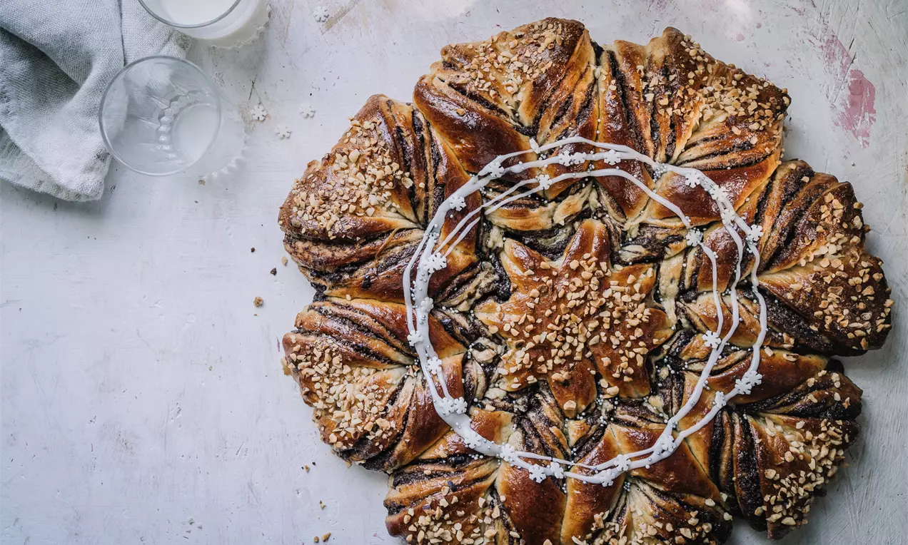 Gyldenbrunt stjerneformet brød med mørke chokoladestriber og hakkede hasselnødder, pyntet med hvid glasur på et lyst bord