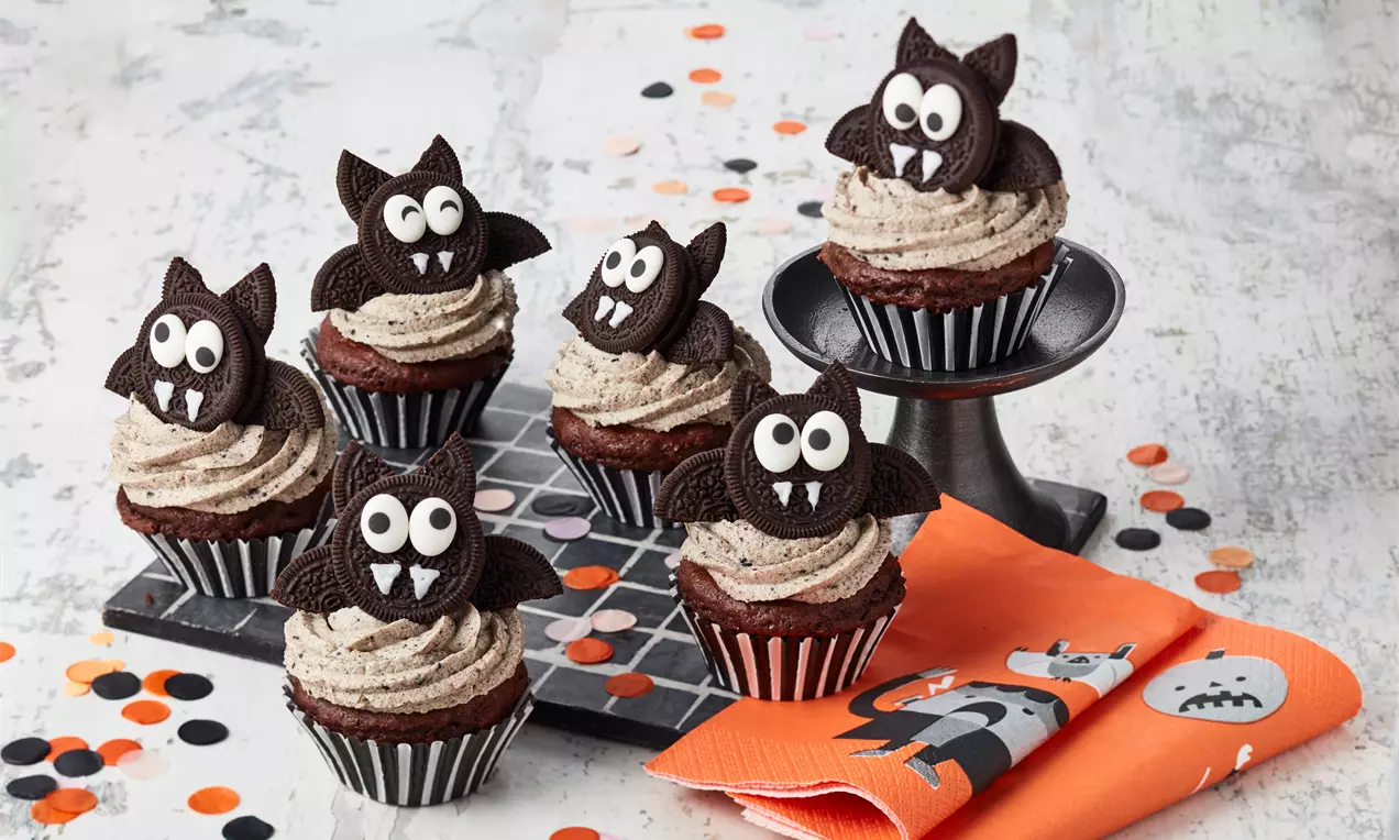 Mørke chokoladecupcakes med stribede forme og grå mousse toppet med flade flagermus lavet af sorte kiks med hvide sukkerøjne