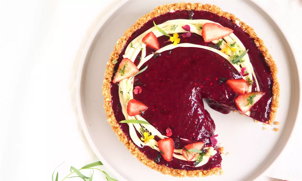 Rødgrød-cheesecake med fyld af blank dybrød frugtgelé toppet med friske jordbær og spiselige blomster på gylden kiksebund