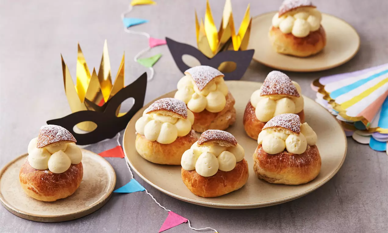 Luftige semlor med gyldenbrune, runde boller fyldt med lys mandelcreme og bærkompot, toppet med flormelis på lyse tallerkener